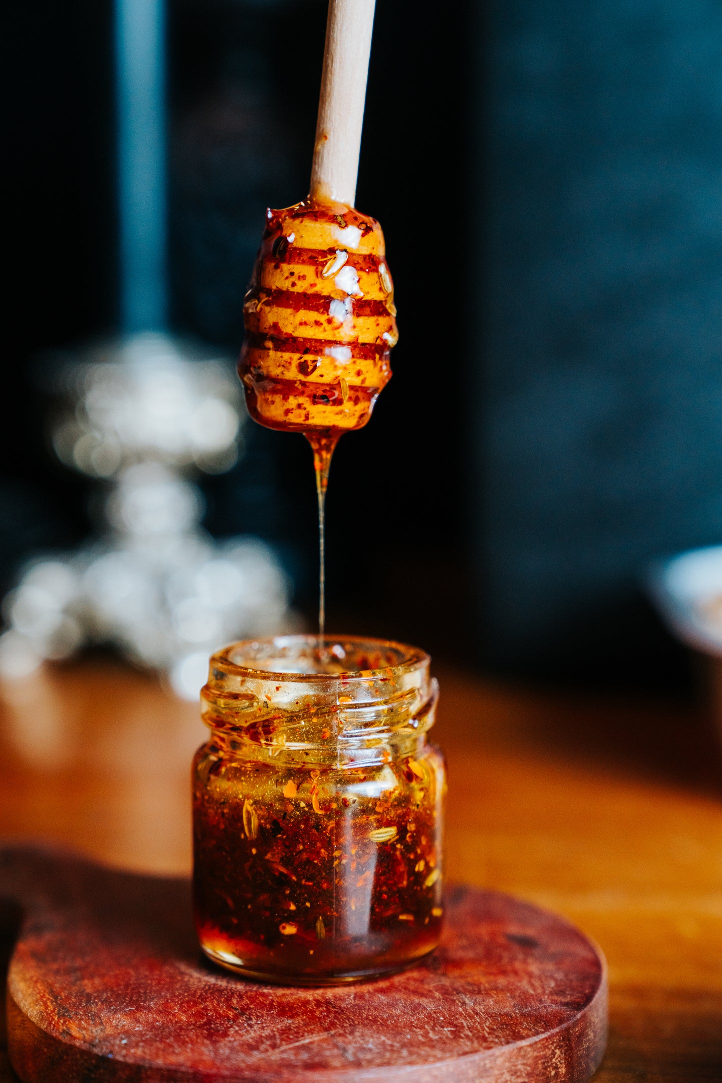 Honey drips from a dipper into a glass jar on a wooden surface with a blurred background.